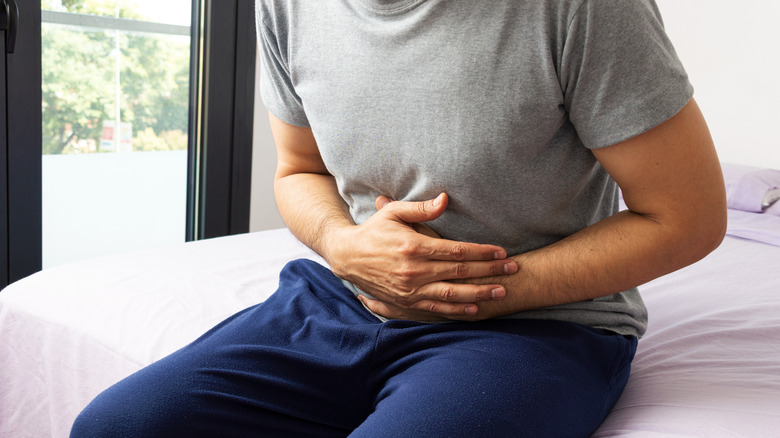 Man sitting on bed and clutching stomach in pain