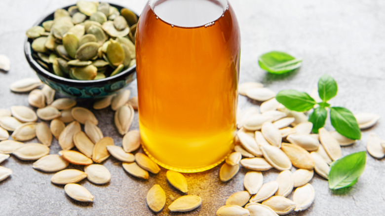 glass jar of pumpkin seed oil surrounded by pumpkin seeds 