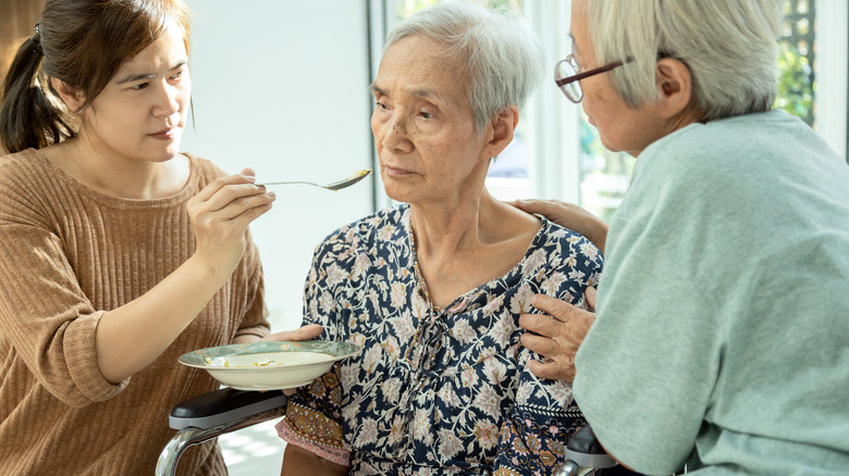 Caretakers spoon feeding elderly woman