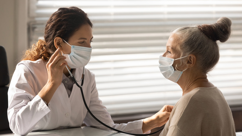 woman doctor listening to older woman's heart