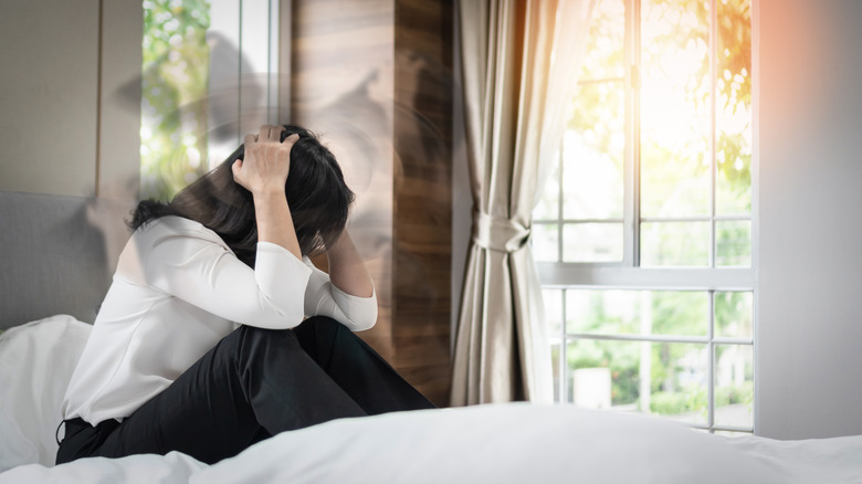 Woman sits in bed with headache