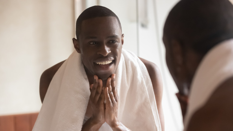 A man touches his face looking in the mirror