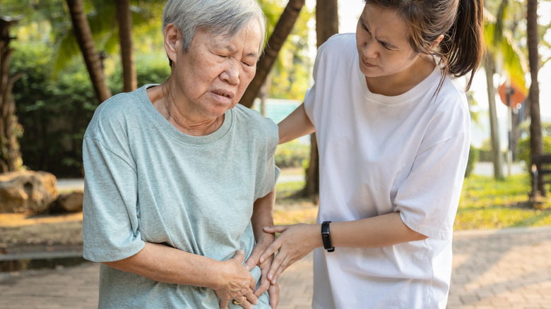 Grimacing senior holding abdomen alongside girl