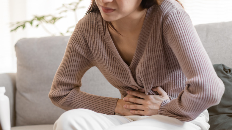 Young woman experiencing abdominal pain, doubled over on couch