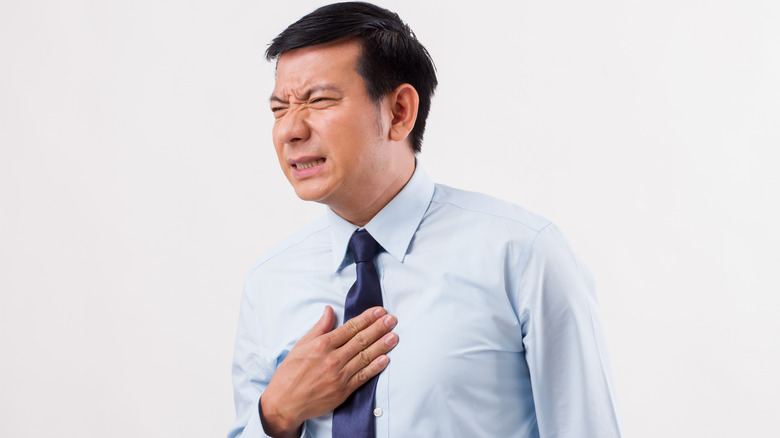 Man in shirt and tie wincing and holding chest in pain