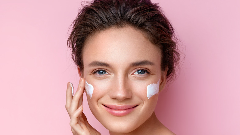 young woman applying moisturizing cream to her cheeks
