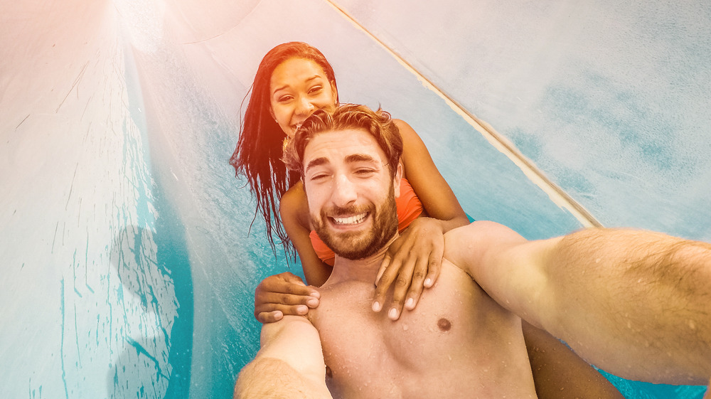 A couple going down a water slide, topless man in front and woman with bikini behind him