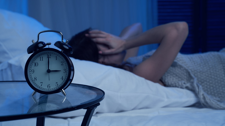 Person unable to sleep in bed, with hands over eyes and alarm clock showing 3 a.m.