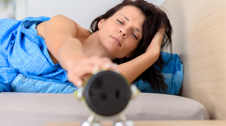Tired woman shutting off alarm clock