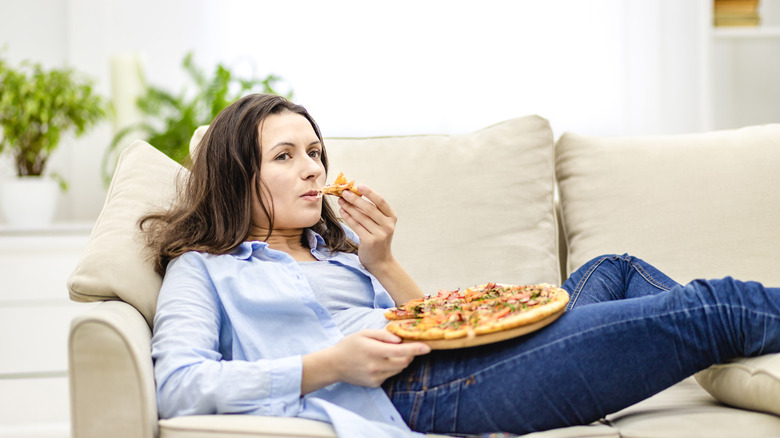 a woman eats pizza on the couch 