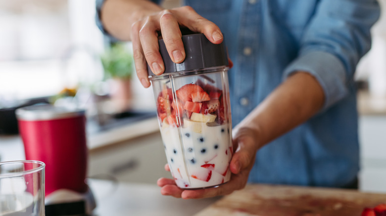 hands holding a smoothie blender with berries