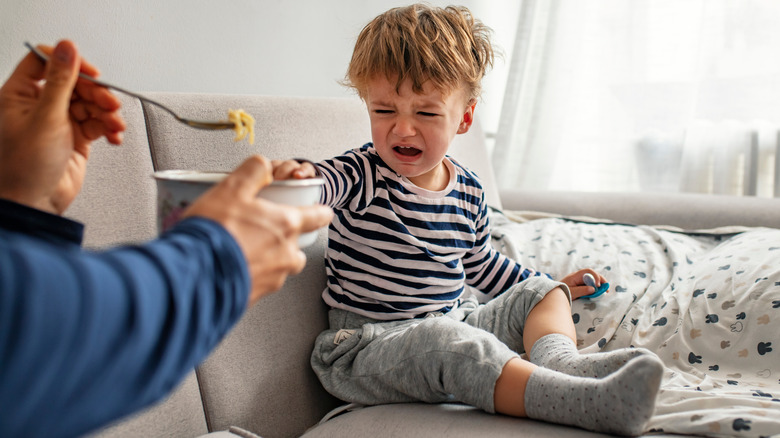 Toddler boy sitting on couch refusing to eat