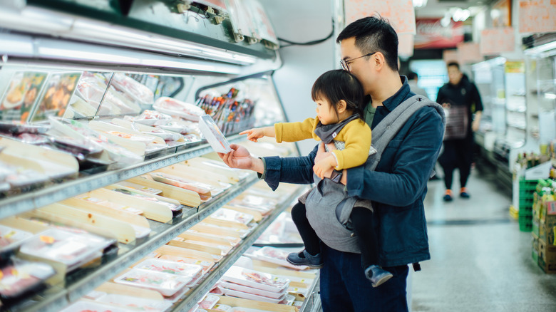 father with daughter choosing chicken parts at the store