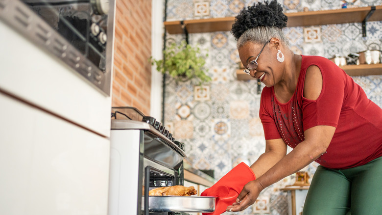 Woman pulling chicken out of oven