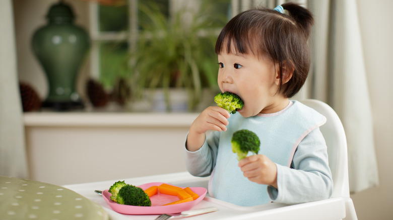 toddler eating broccoli in high chair