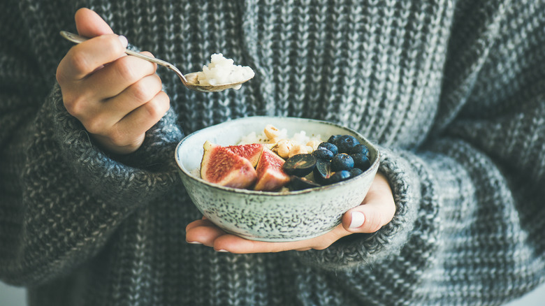 Person in sweater holding bowl of fruit