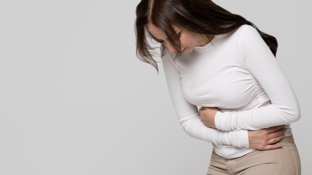 Studio portrait of young woman having a stomachache,from constipation, isolated on grey background