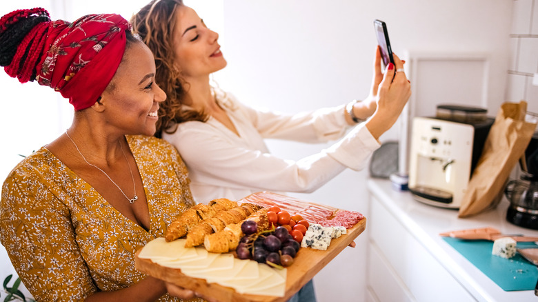 two woman posing with a large cheese board