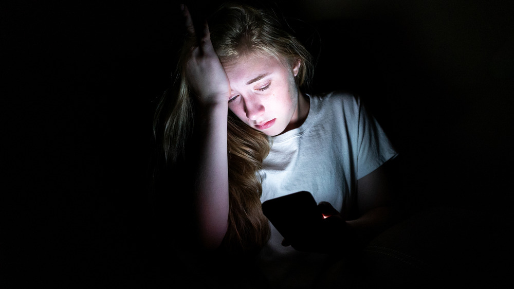Teenager sitting in the dark looking at phone 