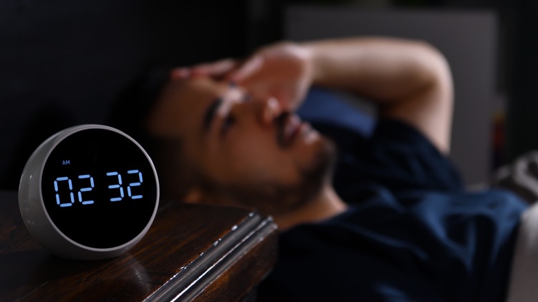 man trying to sleep with an alarm clock on his bedside table