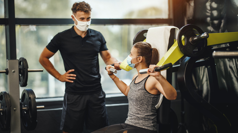 personal trainer aiding client with equipment