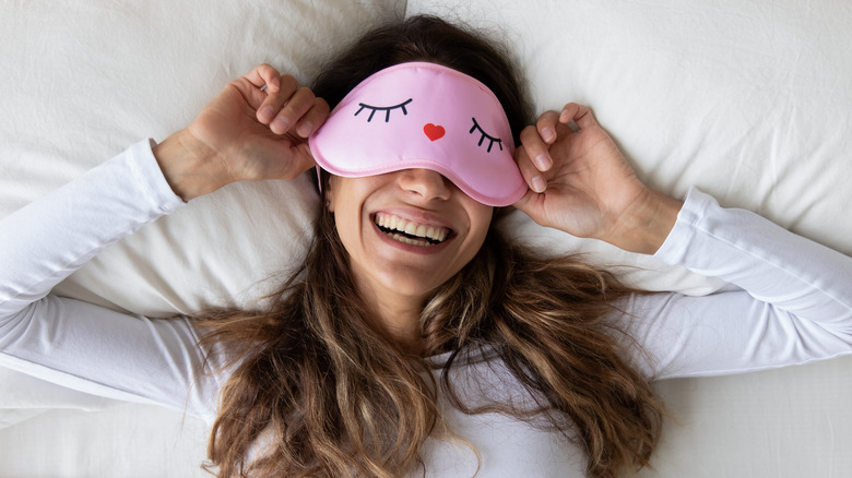 Smiling woman with eye mask in bed