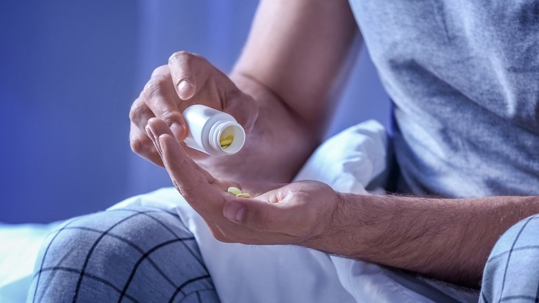 man on bed pours pills into hand