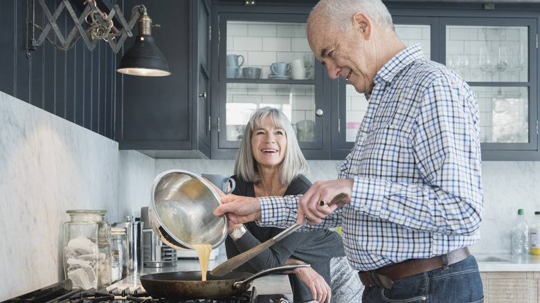 smiling older couple making omelet in kitchen