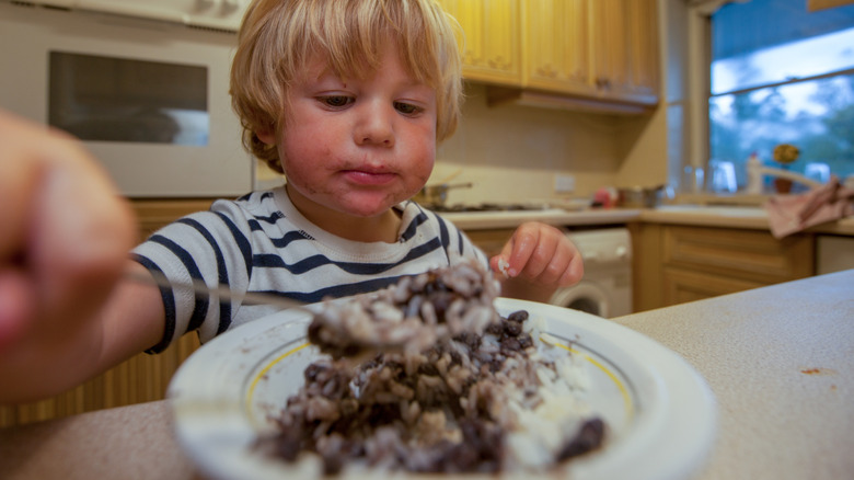 young boy eating rice and beans in kitchen