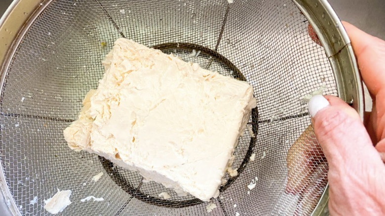 draining tofu in metal sieve