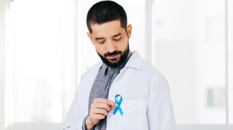 Male doctor looking at blue ribbon on lapel 