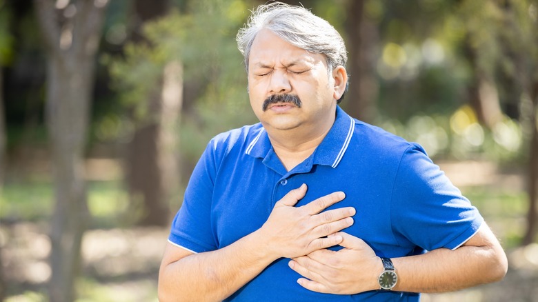 older man grimacing holding left side of chest with 2 hands