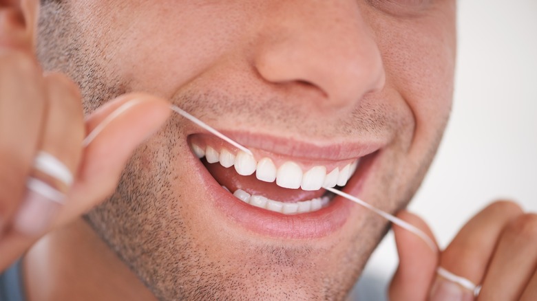 close up of mans mouth while flossing teeth