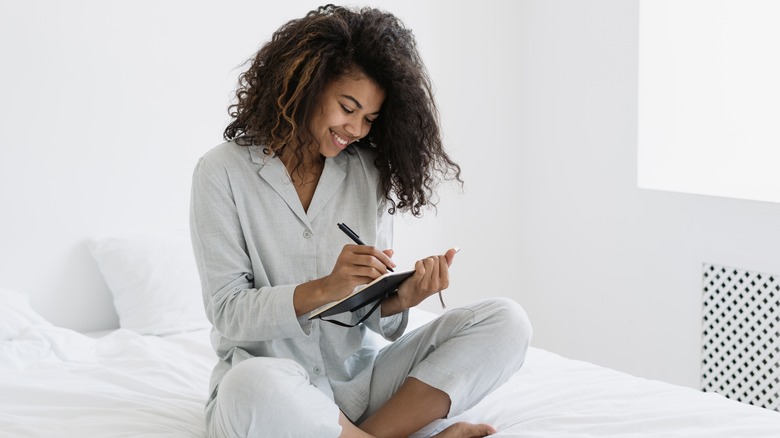 Black woman sitting on bed writing in a book