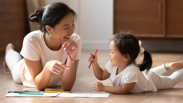 Mom and daughter laying on the floor together drawing with colored pencils