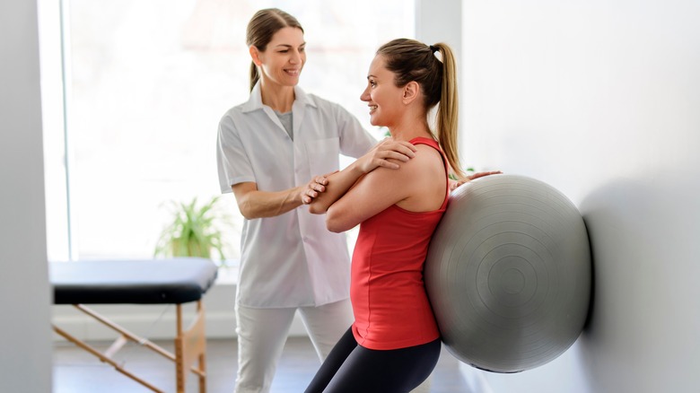 Physiotherapist helping woman will ball exercises