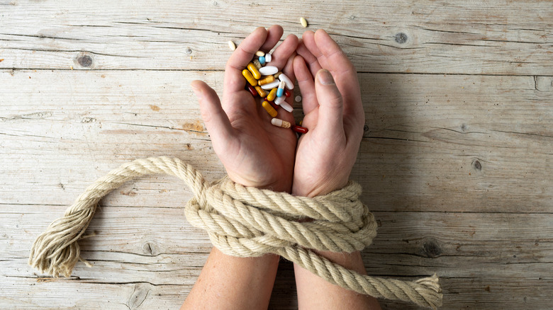 Hands tied with a rope while holding pills