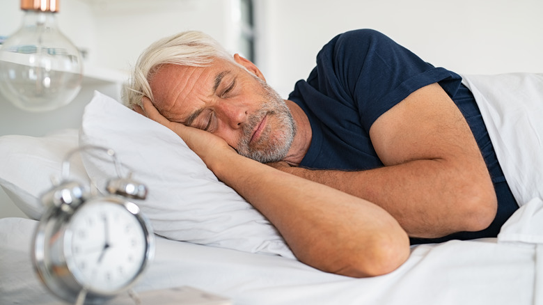 older man sleeping in bed near clock