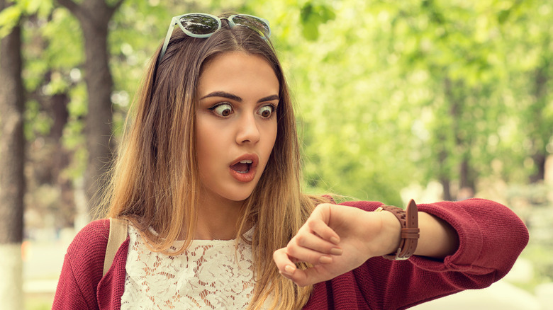 shocked woman checking wristwatch outdoors