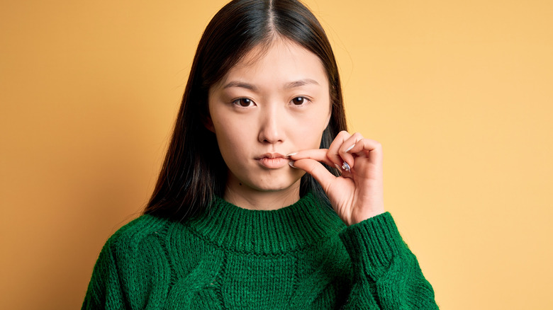 woman zipping mouth with yellow background