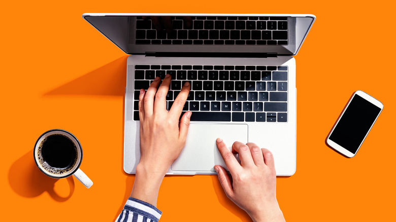 person using laptop with coffee and phone