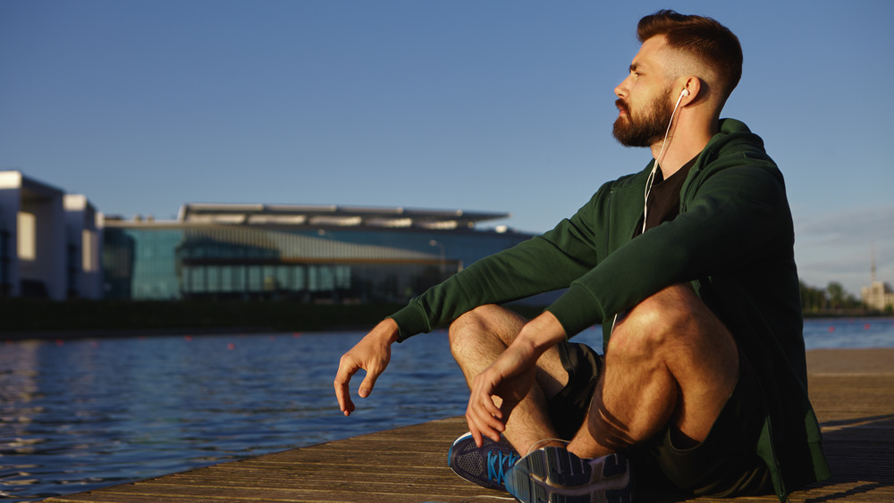 man meditating outside with earbuds on