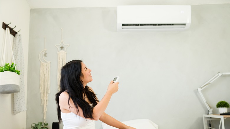 Woman turning on air conditioner in bedroom