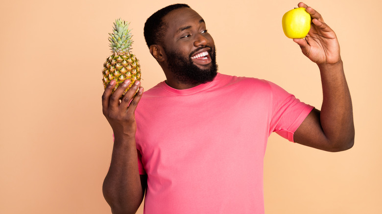 man holding an apple and pineapple