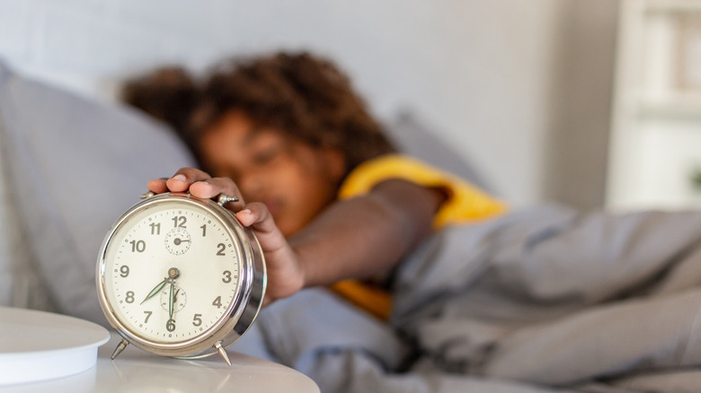 An alarm clock with a woman's hand touching it