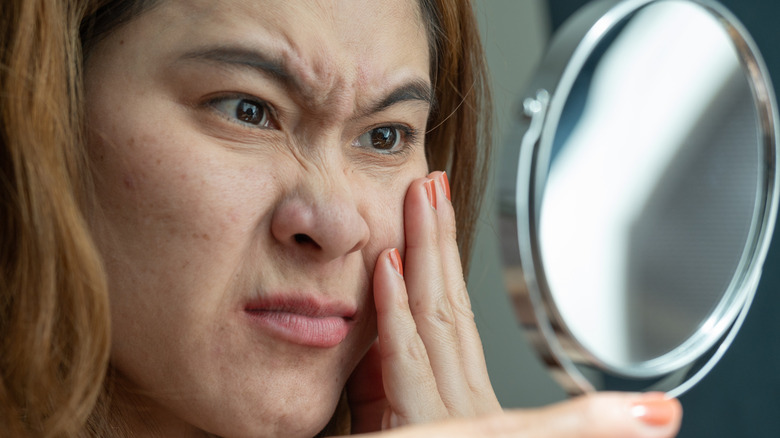 woman looking concerned as she looks in the mirror