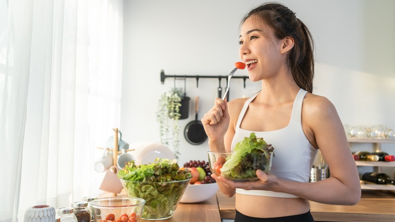 A woman eats a salad in her kitchen 
