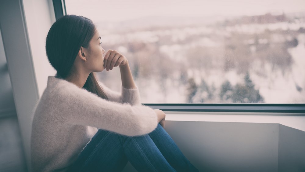 Young woman staring out window with depressed look