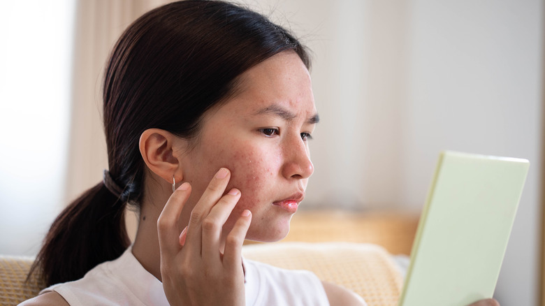 Woman looking in mirror concerned about acne