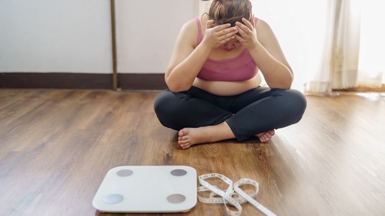 Woman sitting by scale upset with weight